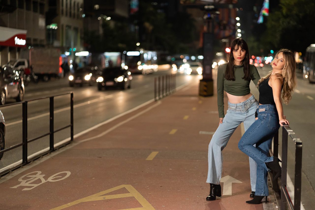 Two women posing on a bicycle lane downtown, showcasing urban fashion at night.