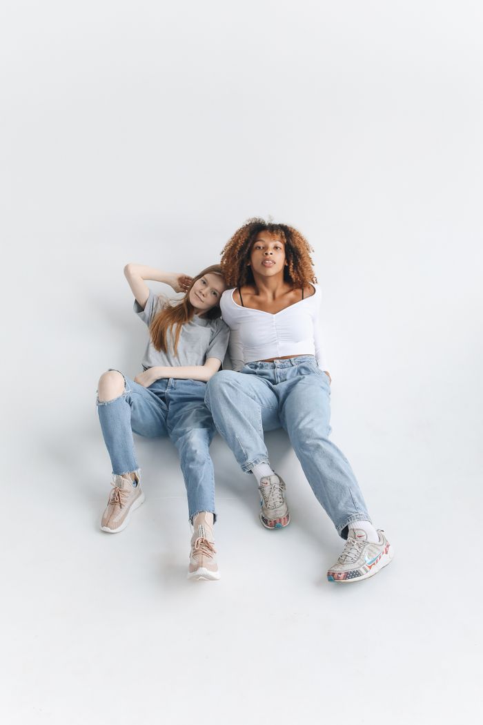Two young women in casual attire sitting together, showcasing friendship and diversity.