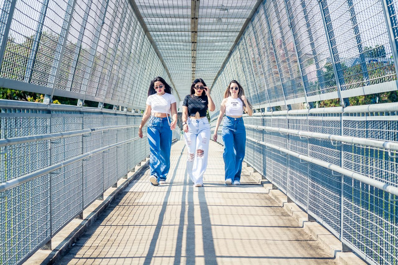 Three stylish women walking confidently on a sunlit bridge in Sorocaba, Brazil.